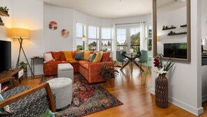 Ein modernes Wohnzimmer mit einem Ecksofa, einem Esstisch mit Stühlen, einem Fernseher und einem großen Spiegel.