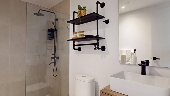 Ein modernes Badezimmer mit Duschkabine aus Glas, einer weißen Toilette, einer weißen Badewanne und schwarzen, schwebenden Ablageflächen mit Toilettenartikeln.