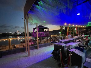 Ein Außenbar-Bereich mit Blick auf einen Pool, ein überdachter Sitzbereich und eine Bühne.