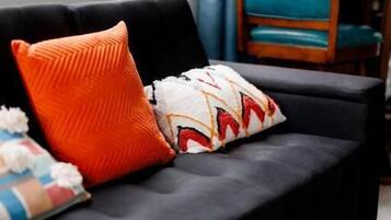A dark-colored sofa with two pillows, a wooden chair, and a dining table with a blue bowl.
