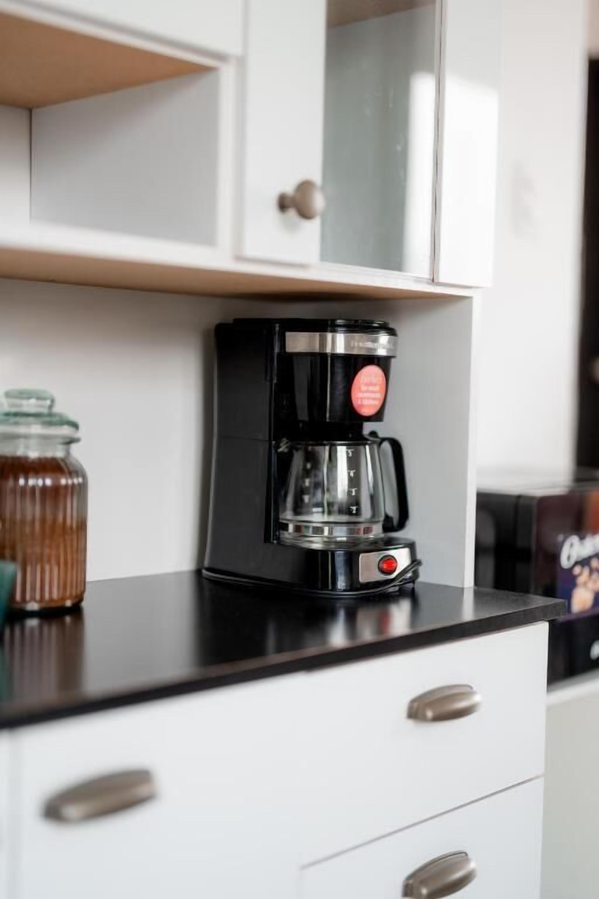 Una cocina con cafetera en la encimera, un tarro de miel y un refrigerador.