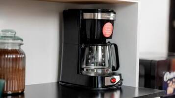 Una cocina con cafetera en la encimera, un tarro de miel y un refrigerador.