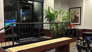 A billiards table, chairs, a potted plant, a framed picture, and a glass door with a view.