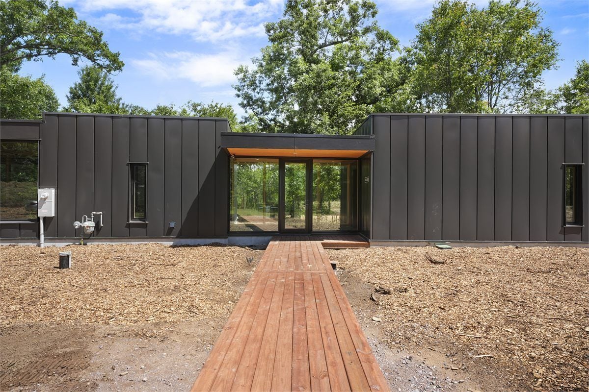 A modern building with a wooden deck leading to a glass entrance, surrounded by trees.