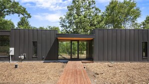Un edificio moderno con una terrazza in legno che conduce all'ingresso in vetro, immerso nel verde.