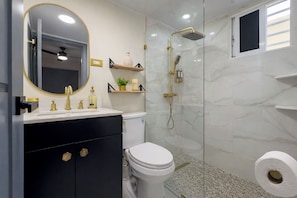 Une salle de bain équipée de toilettes, d’un lavabo, d’un miroir, d’une douche et dont les murs sont recouverts de marbre.