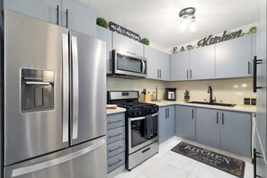 A modern kitchen with stainless steel appliances, grey cabinets, and a black and white backsplash. - Modern condo 1st floor+pool+playground & 24/7Security (La Romana)