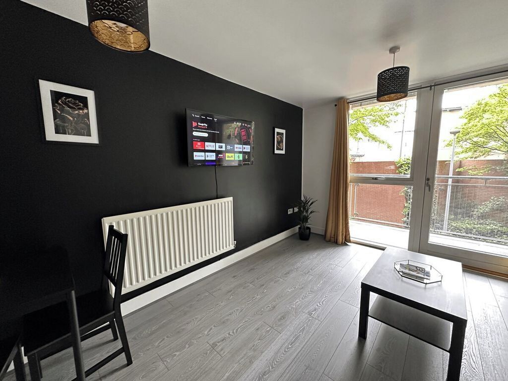A modern living room with a black wall, a mounted TV, a radiator, a window with curtains, and a dining area with a table and chairs.