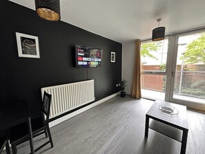 Un salon moderne avec un mur noir, un téléviseur fixé au mur, un radiateur, une fenêtre avec des rideaux et un coin repas comprenant une table et des chaises.