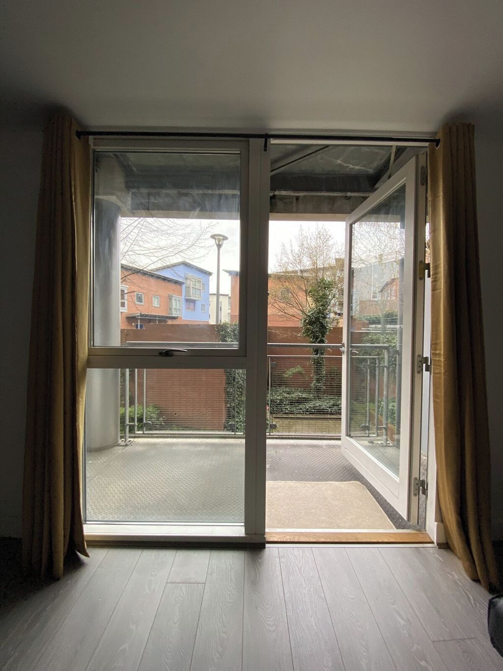 A room with a sliding glass door leading to a balcony with a view of buildings and a fence.