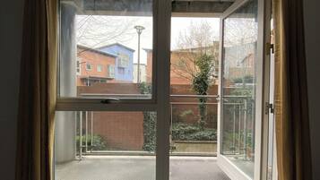 A room with a sliding glass door leading to a balcony with a view of buildings and a fence.