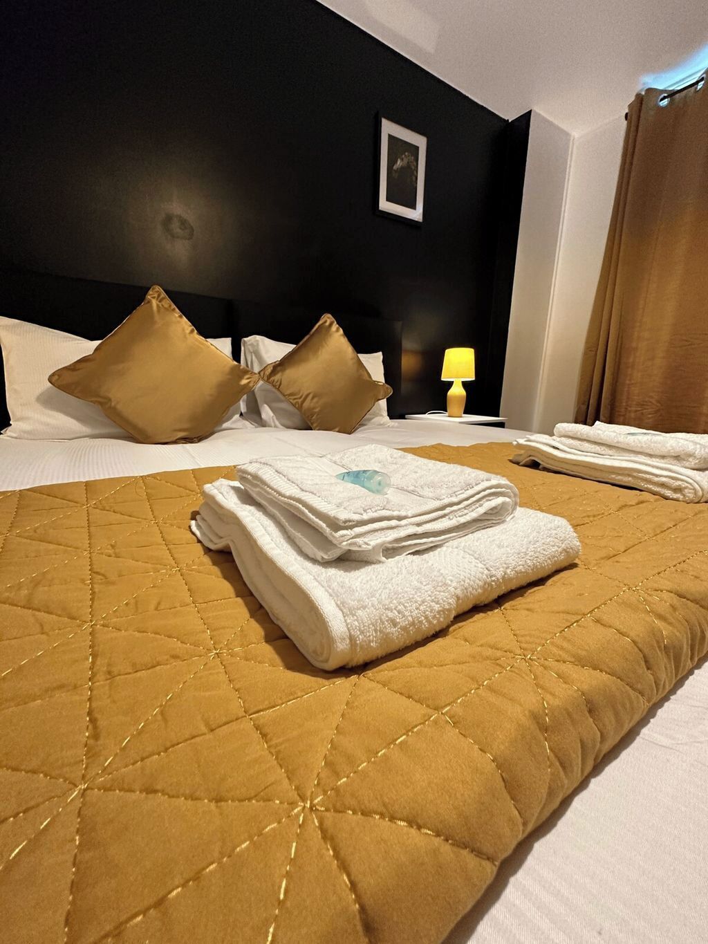 A neatly made bed with a quilted headboard, pillows, and folded towels.