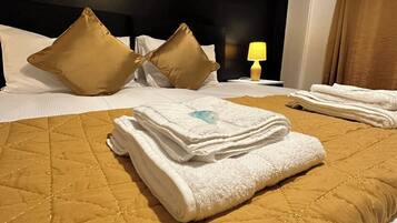 A neatly made bed with a quilted headboard, pillows, and folded towels.