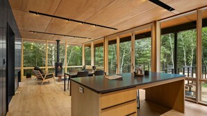 Een moderne keuken met een groot kookeiland, houten vloeren en grote ramen met uitzicht op het bos.