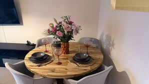 A round wooden dining table with four chairs, a vase with flowers, and wine glasses. - City Center Gem Steps from Albert Clock &Cathedral (Belfast)