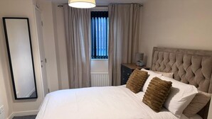 A neatly made bed with a headboard, two pillows, a bedside table with a lamp, and a window with curtains. - City Center Gem Steps from Albert Clock &Cathedral (Belfast)