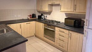 A kitchen with wooden cabinets, a gas stove, a microwave, and a sink. - City Center Gem Steps from Albert Clock &Cathedral (Belfast)