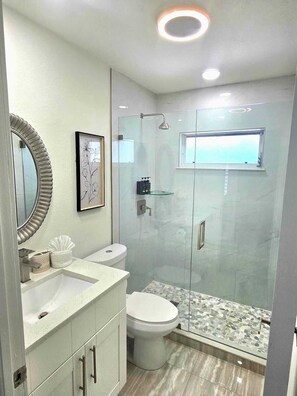 Ein modernes Badezimmer mit einer gläsernen Duschkabine, einer Toilette, einem Waschbecken mit Spiegel und einem gerahmten Bild an der Wand.