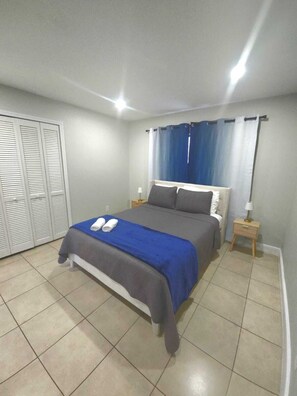 Une chambre à coucher comprenant un lit, deux tables de chevet, une commode, une armoire et une fenêtre avec des rideaux.