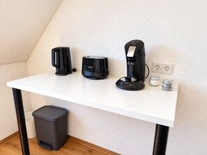 Ein weißer Schreibtisch mit drei Kaffeemaschinen, einem Mülleimer und einer Steckdose.