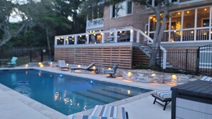 A swimming pool with lounge chairs and a deck area with lights. - Fall for Canal Breeze: Private Lot on the Canal, Saltwater Pool; Dock; Beach! (Oak Island)