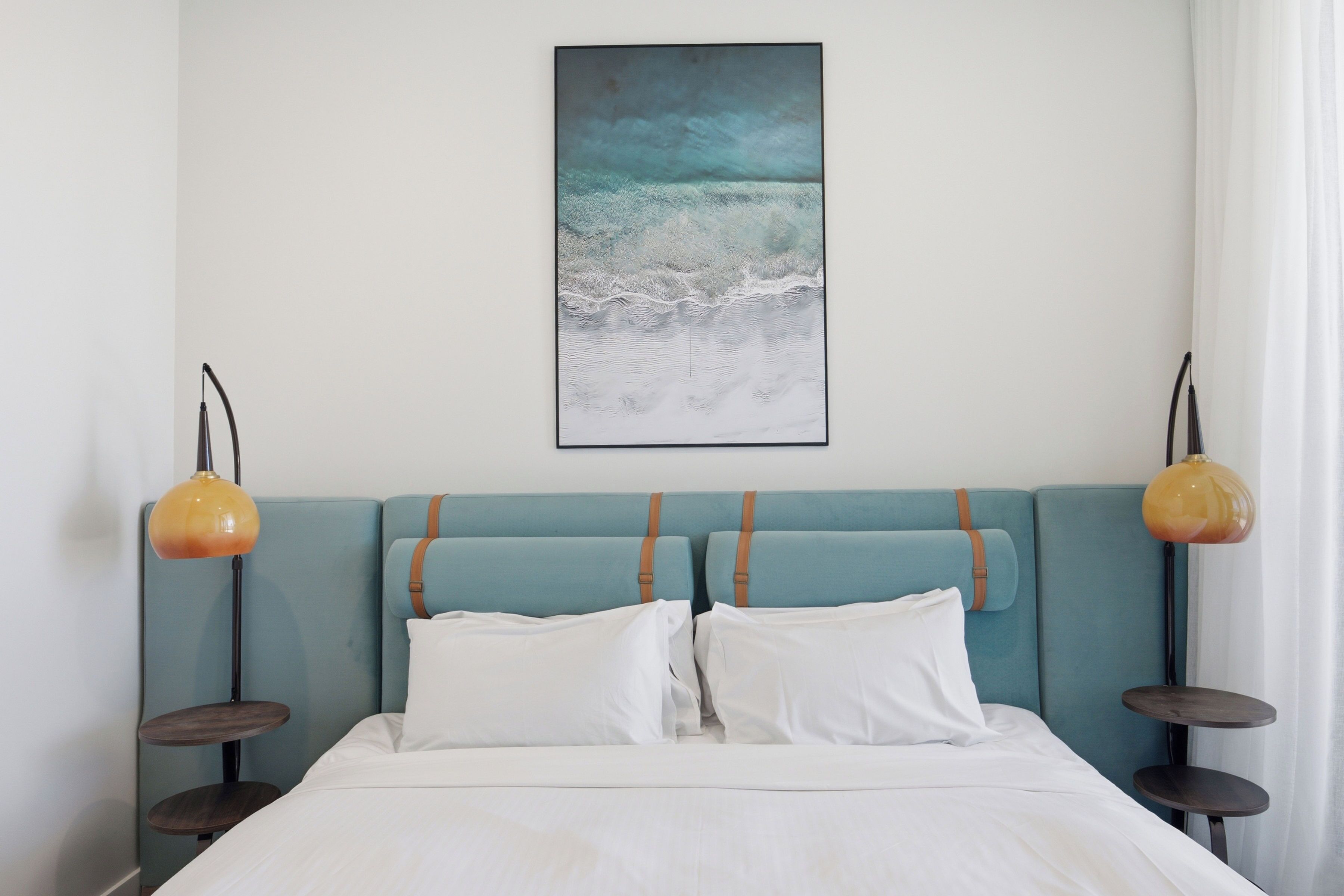 Un lit avec du linge de lit blanc, une tête de lit turquoise et deux lampes de chevet.