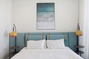 Una cama con sábanas blancas, cabecera color aguamarina y dos lámparas de noche.