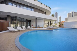 A modern building with a rooftop swimming pool, lounge chairs, and a view of the city skyline. - Chevron One Residences (Surfers Paradise)