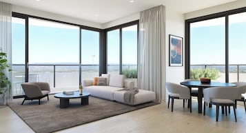A modern living room with a sofa, chairs, a coffee table, and a dining table. Large windows offer a view of the cityscape.
