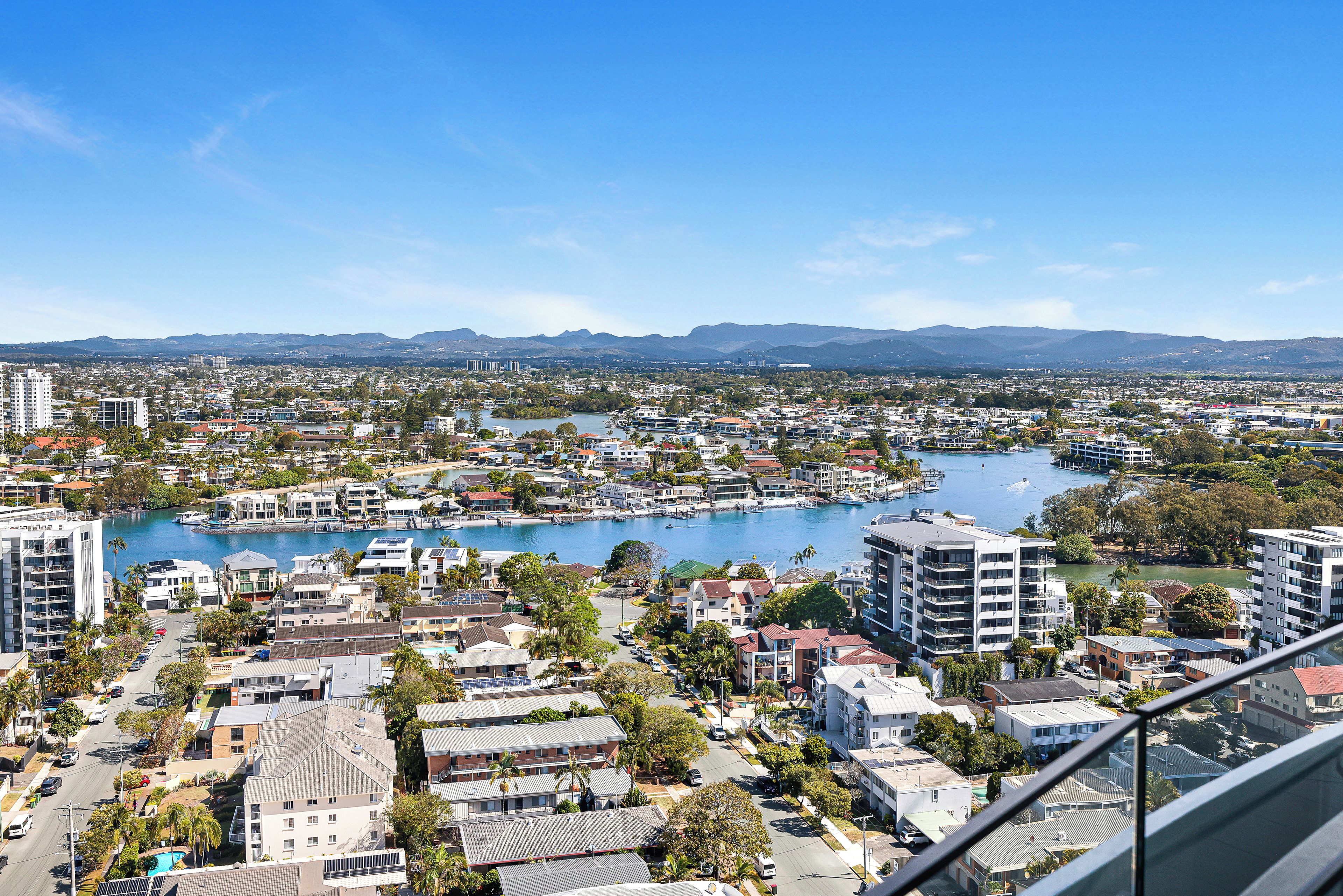 Un paysage urbain côtier avec des immeubles résidentiels, une marina et une chaîne de montagnes à l’horizon.