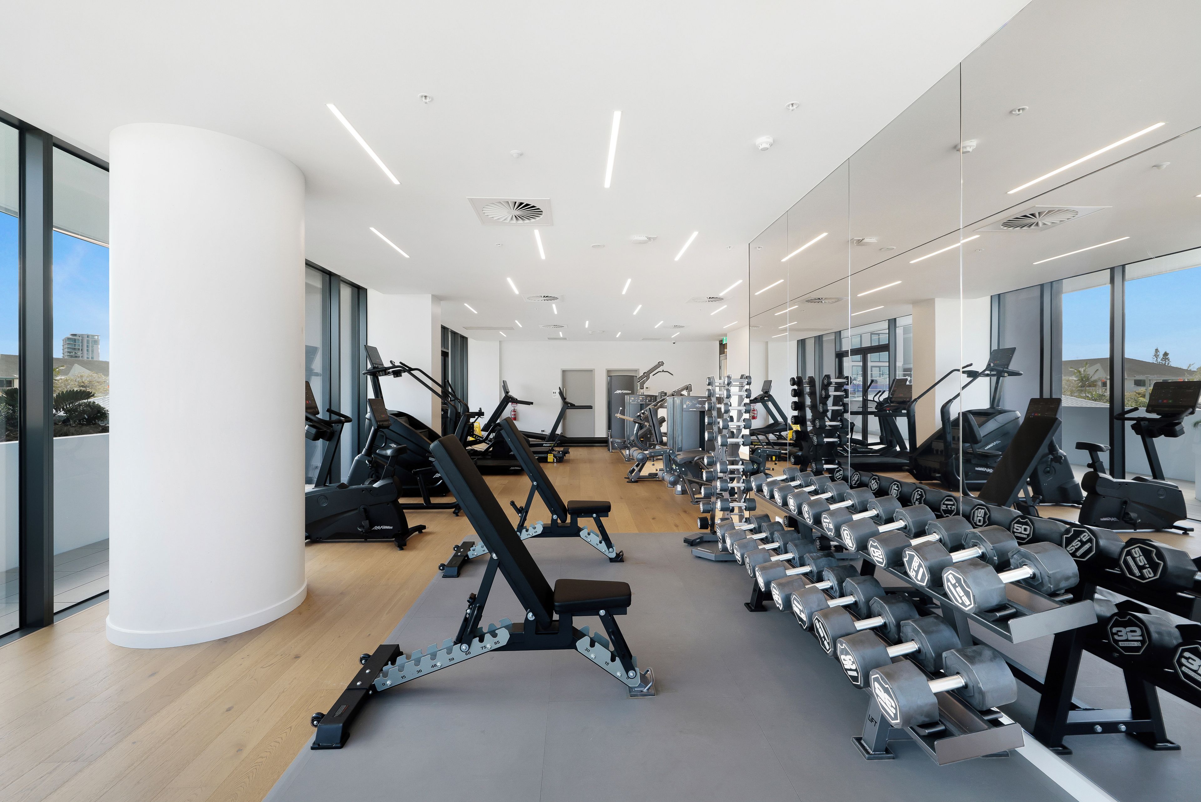 A modern gym with various exercise equipment, large windows, and a clean, spacious layout.