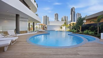 A modern pool area with lounge chairs, a wooden deck, and a city skyline in the background.