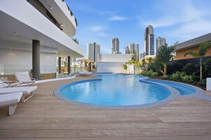 Un área de piscina moderna con sillones, una terraza de madera y un horizonte urbano al fondo.