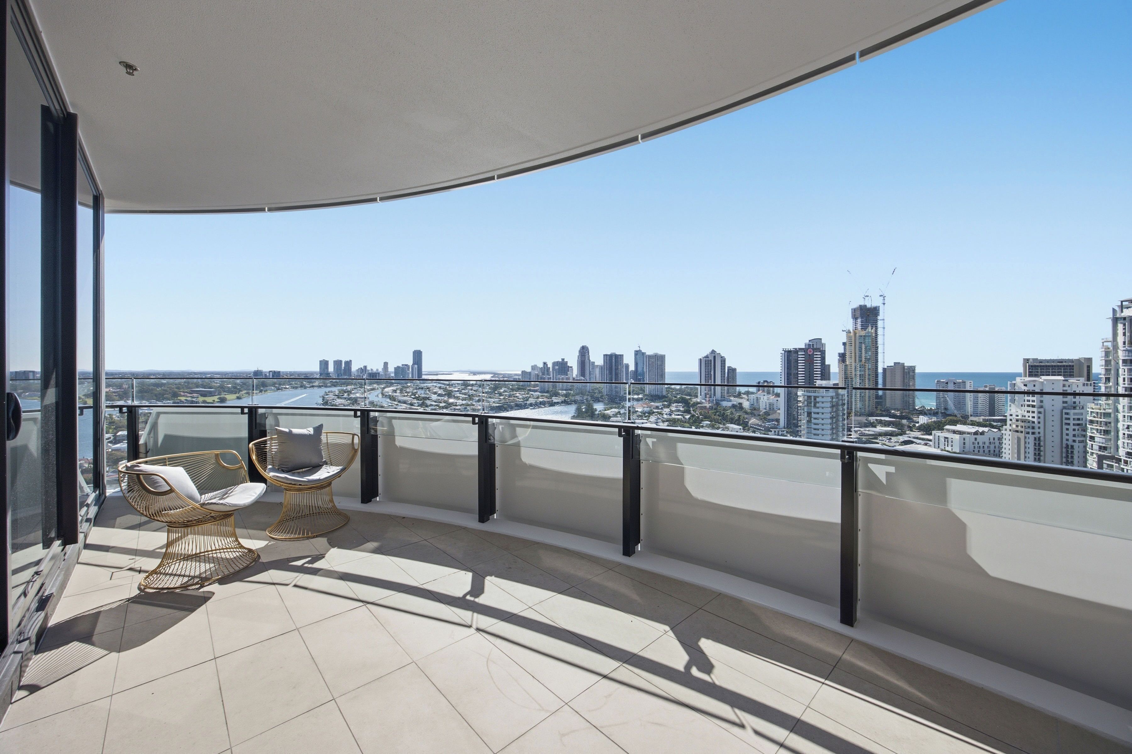 A balcony with a view of a city skyline, two wicker chairs, and a glass railing.
