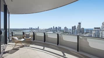 A balcony with a view of a city skyline, two wicker chairs, and a glass railing.