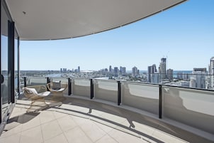 A balcony with a view of a city skyline, two wicker chairs, and a glass railing.