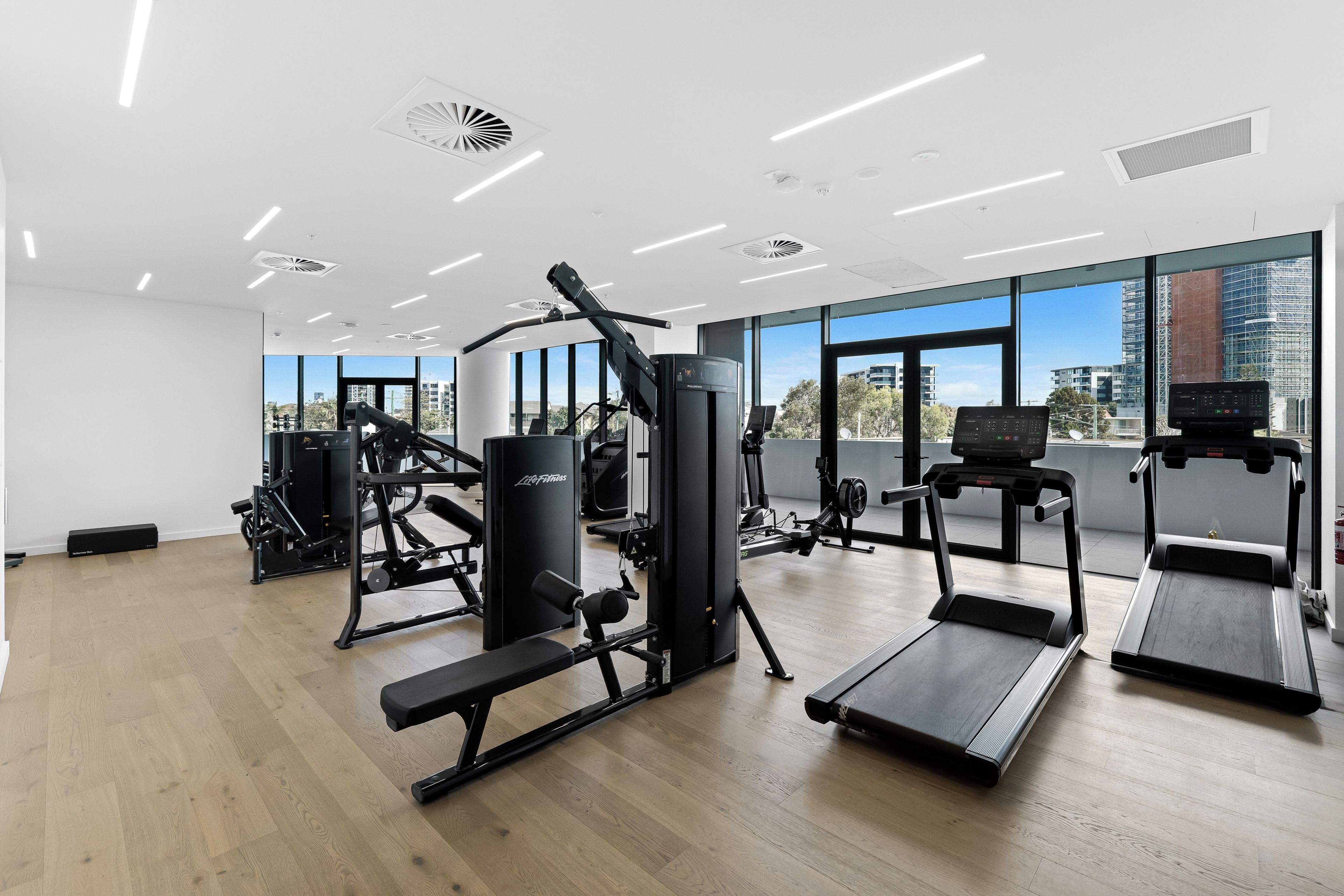 A gym with exercise equipment, large windows, and a view of buildings.