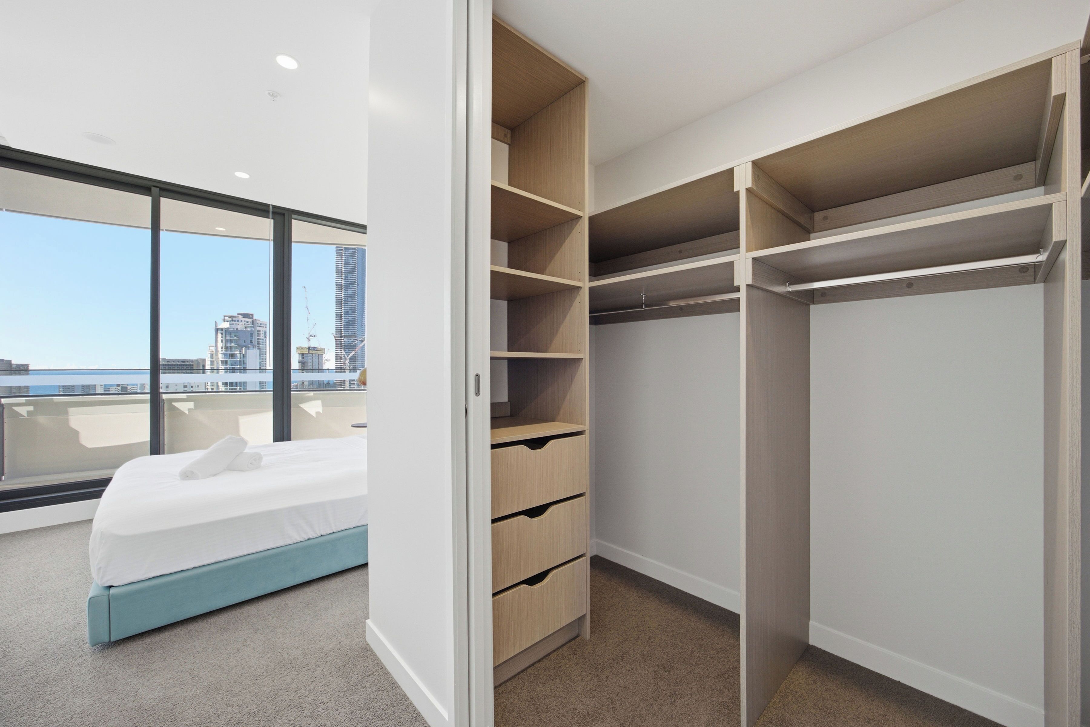 Quarto com cama, uma janela grande e um guarda-roupa com várias prateleiras e gavetas.