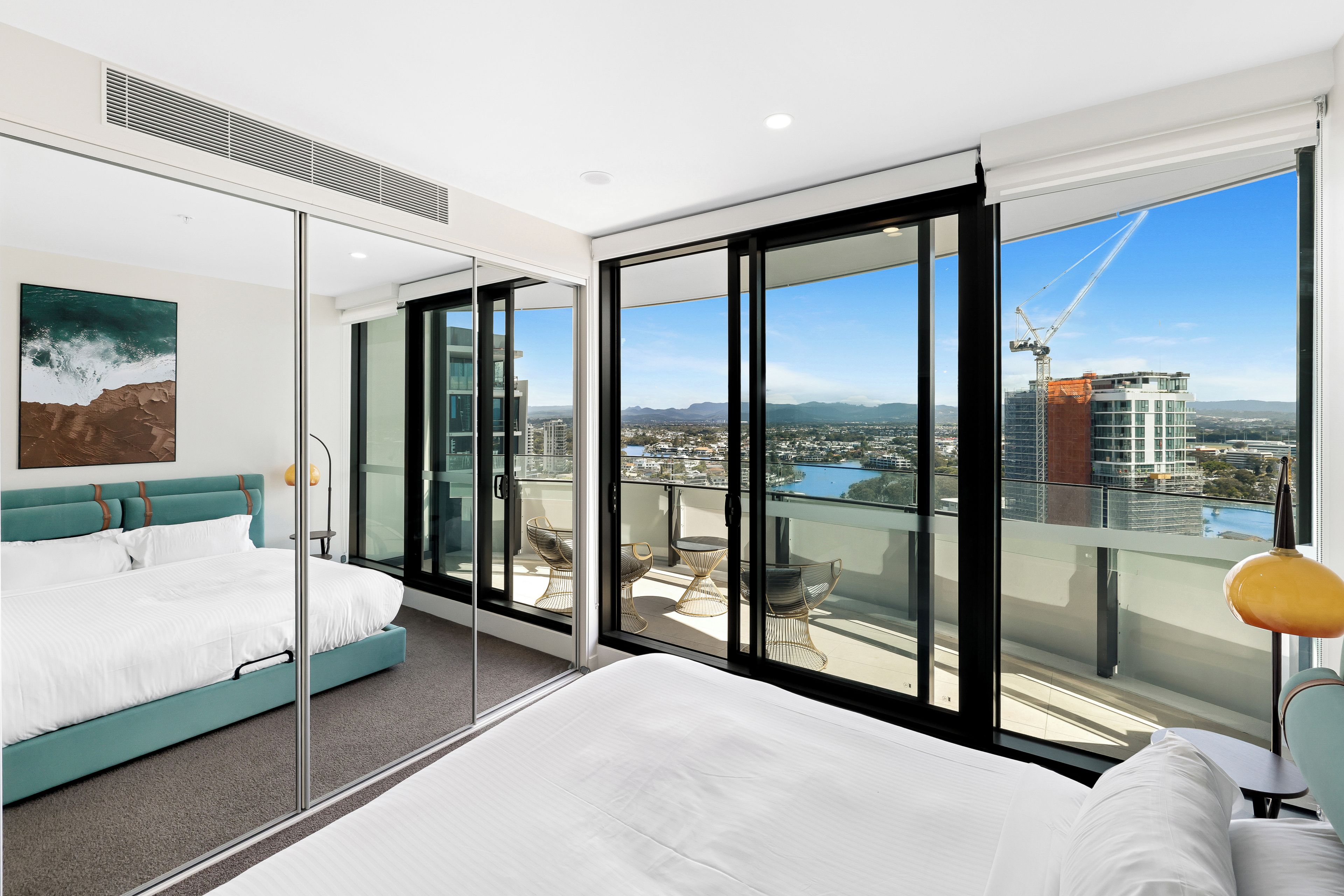 A modern hotel room with a large bed, a view of the cityscape, and a balcony with outdoor furniture.