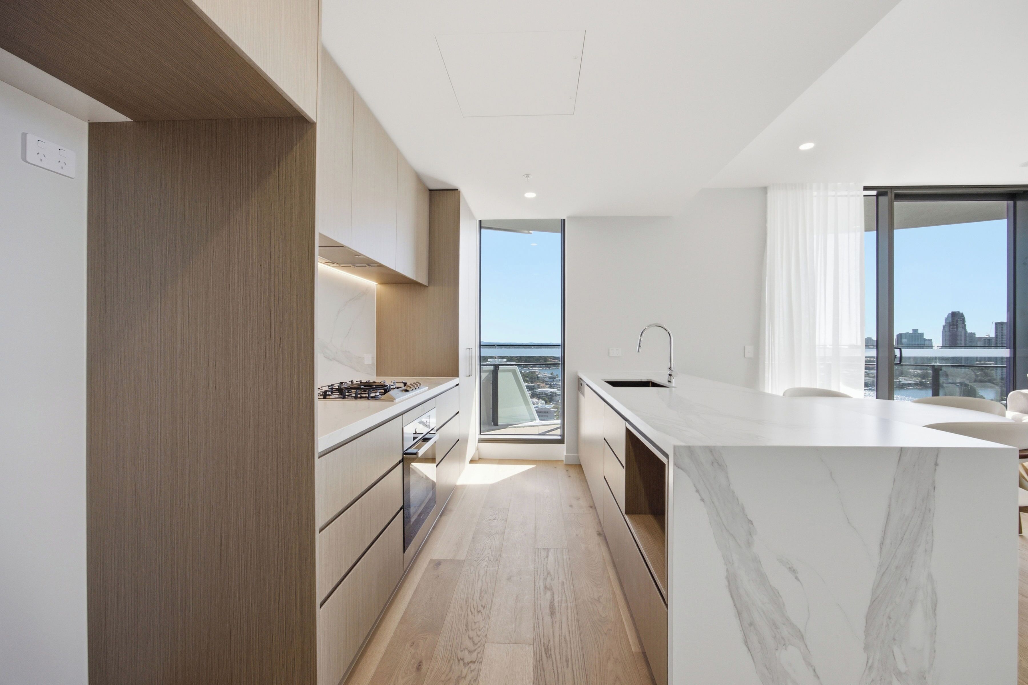 A modern kitchen with a large island, wooden cabinetry, and a view of the city.