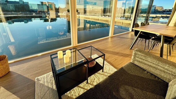 A modern living room with large windows, a glass coffee table, and a dining area.