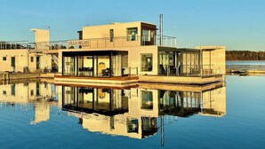 A modern floating hotel with a glass facade, a deck area, and a clear view of the water.