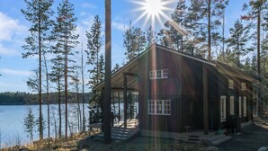 A cabin with a deck overlooking a lake, surrounded by trees.