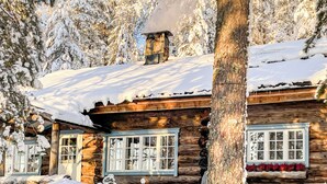Eine Blockhütte mit Schornstein, Fenstern und verschneiter Umgebung.