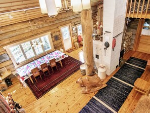 A wooden cabin interior with a dining area, large windows, and a fireplace.