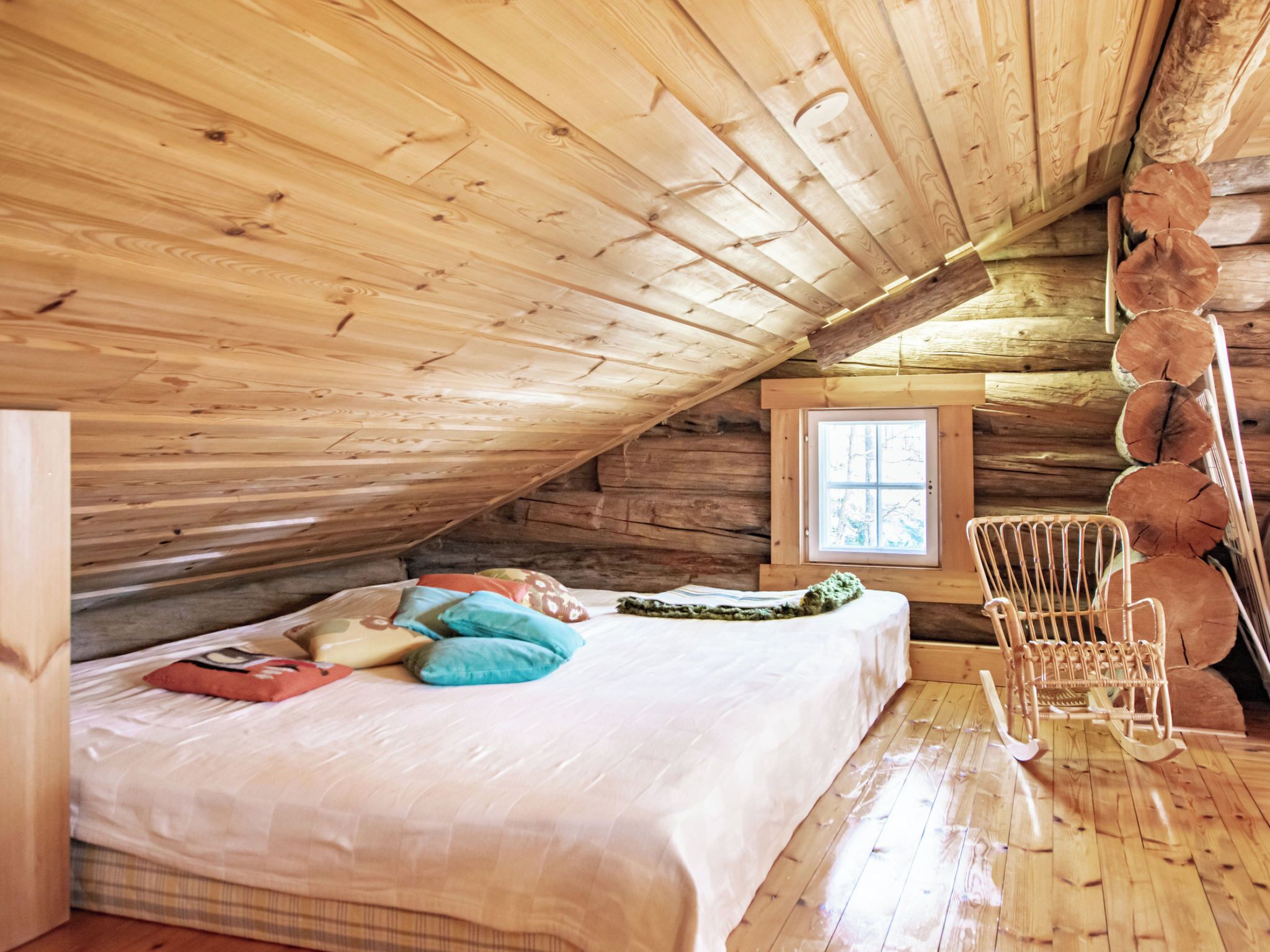 Une cabane en bois avec une chambre à coucher située en mezzanine, un lit avec des oreillers, un fauteuil à bascule et une fenêtre.