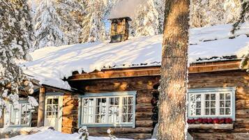 A log cabin with a chimney, windows, and snow-covered surroundings.