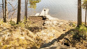 Eine Holztreppe führt zu einem Steg über dem Wasser, umgeben von Bäumen und felsigem Gelände.