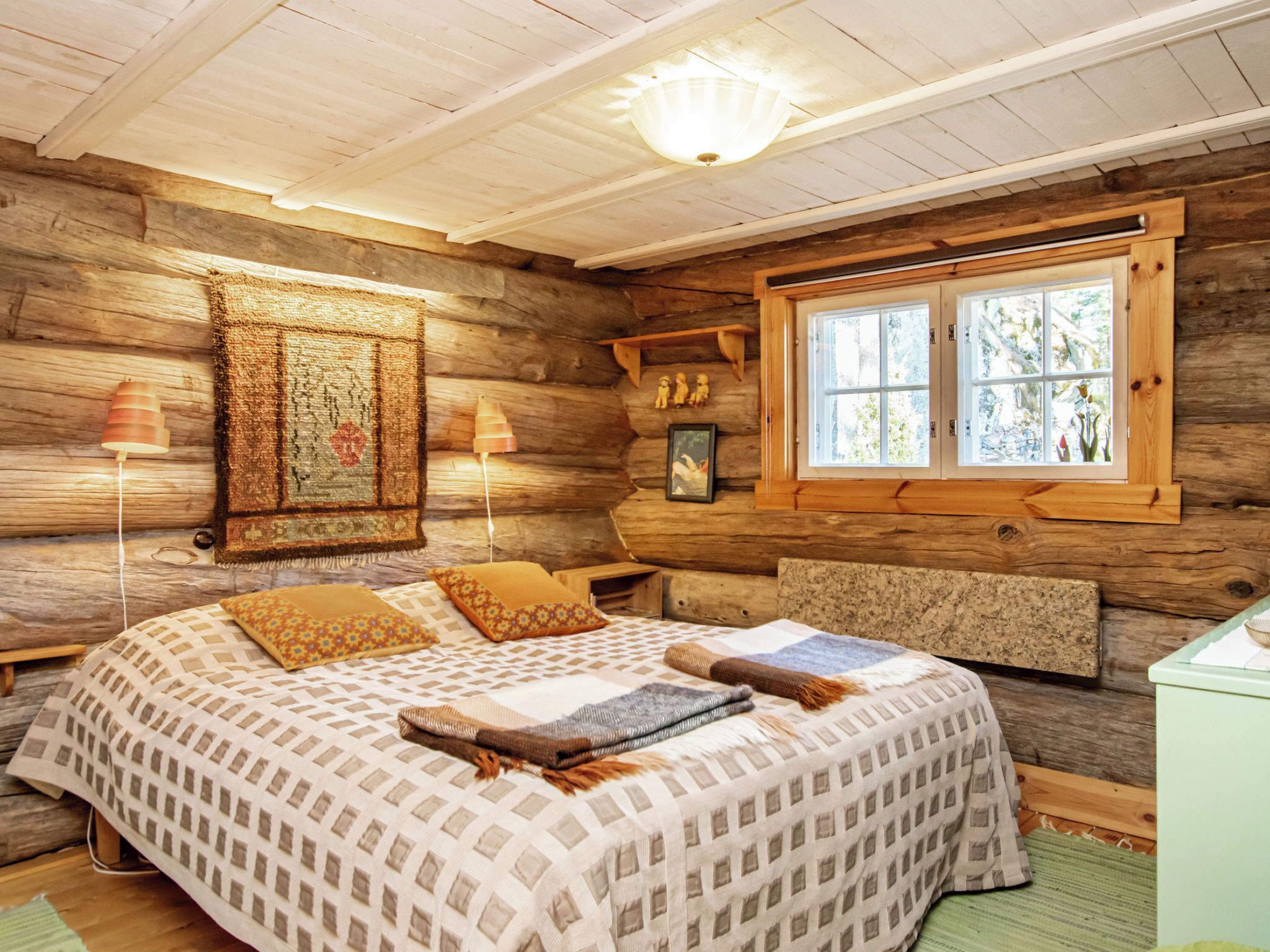 Un dormitorio de cabaña de troncos con una cama, dos lámparas, una ventana y un muro de madera.
