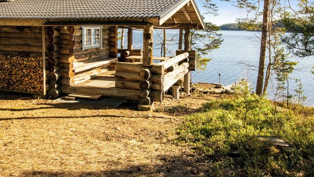 Eine Blockhütte mit Veranda mit Blick auf einen See, umgeben von Bäumen.